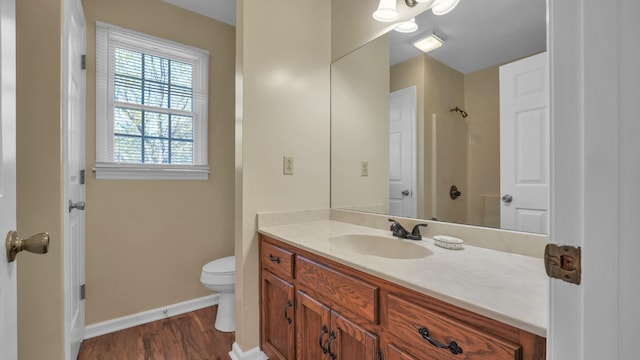 bathroom with vanity, toilet, a shower, wood finished floors, and baseboards