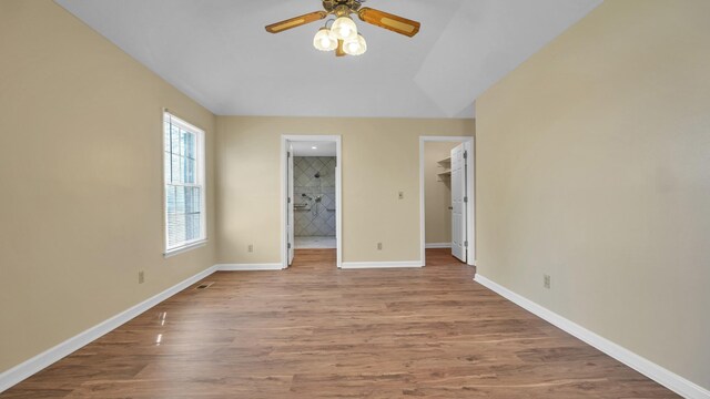 unfurnished bedroom with a closet, baseboards, a spacious closet, ensuite bath, and wood finished floors