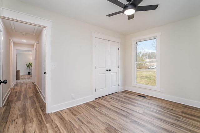 unfurnished bedroom featuring visible vents, a closet, baseboards, attic access, and wood finished floors