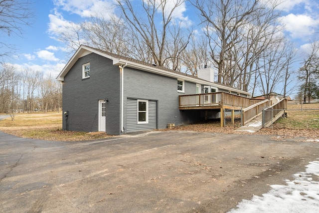 back of property featuring aphalt driveway, brick siding, a wooden deck, and a chimney