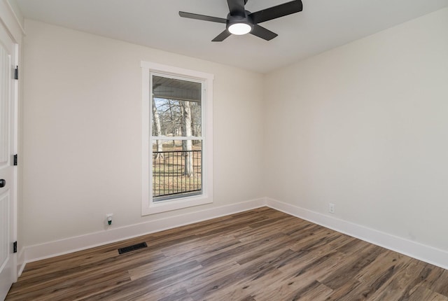 empty room featuring dark wood-style flooring, baseboards, a ceiling fan, and visible vents