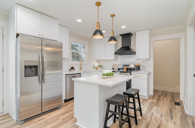 kitchen with crown molding, wall chimney range hood, white cabinets, a sink, and stainless steel appliances