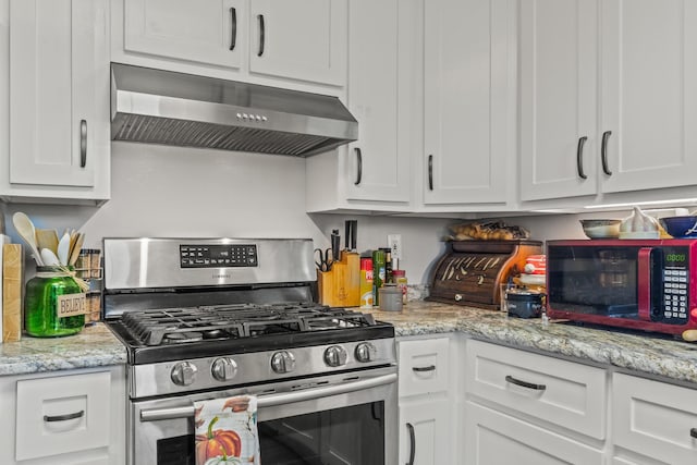 kitchen featuring stainless steel gas range, white cabinetry, light stone counters, and under cabinet range hood