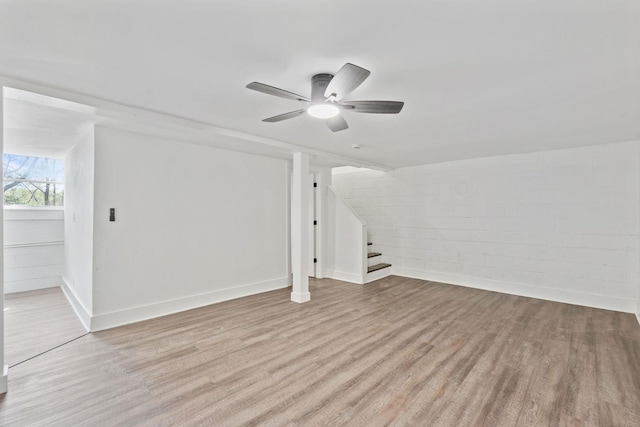 additional living space with wood finished floors, ceiling fan, concrete block wall, and stairs