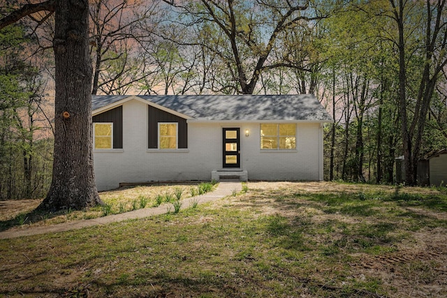 single story home with brick siding, a front yard, entry steps, and roof with shingles
