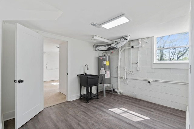 below grade area with water heater, visible vents, concrete block wall, and wood finished floors