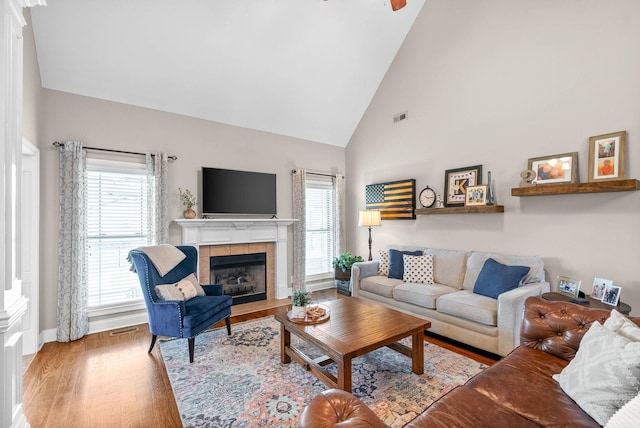 living area with visible vents, wood finished floors, a tile fireplace, and a healthy amount of sunlight