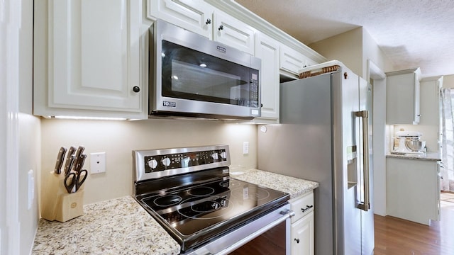 kitchen with white cabinetry, appliances with stainless steel finishes, wood finished floors, and light stone countertops