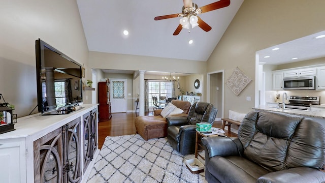 living room featuring decorative columns, recessed lighting, ceiling fan with notable chandelier, light wood-style flooring, and high vaulted ceiling