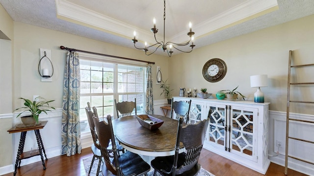 dining space featuring ornamental molding, a chandelier, wainscoting, a raised ceiling, and wood finished floors