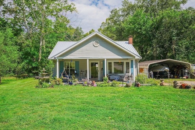 back of house featuring a detached carport, a chimney, a porch, a yard, and metal roof