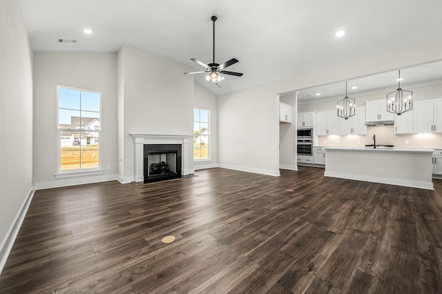 unfurnished living room featuring visible vents, a fireplace with flush hearth, baseboards, ceiling fan with notable chandelier, and dark wood-type flooring