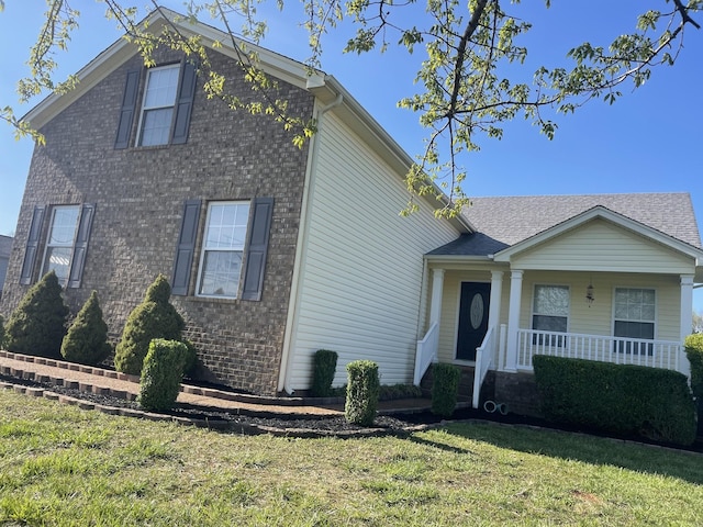 view of front of home featuring brick siding, a front lawn, and covered porch