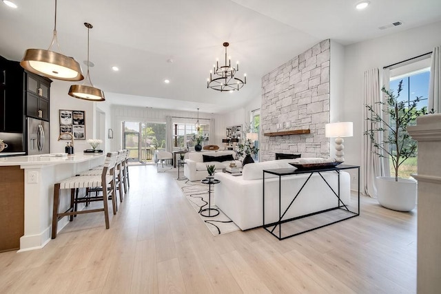 living area with visible vents, an inviting chandelier, a stone fireplace, recessed lighting, and light wood finished floors