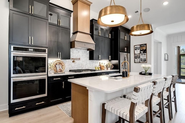 kitchen featuring a center island with sink, tasteful backsplash, dark cabinets, a sink, and stainless steel appliances
