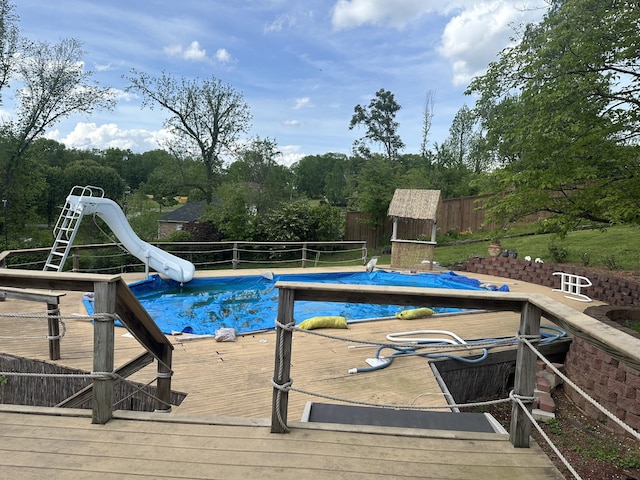 view of swimming pool featuring a water slide, a fenced backyard, and a deck