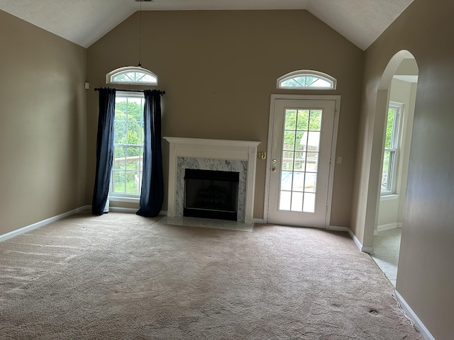 unfurnished living room with carpet, a premium fireplace, healthy amount of natural light, arched walkways, and high vaulted ceiling
