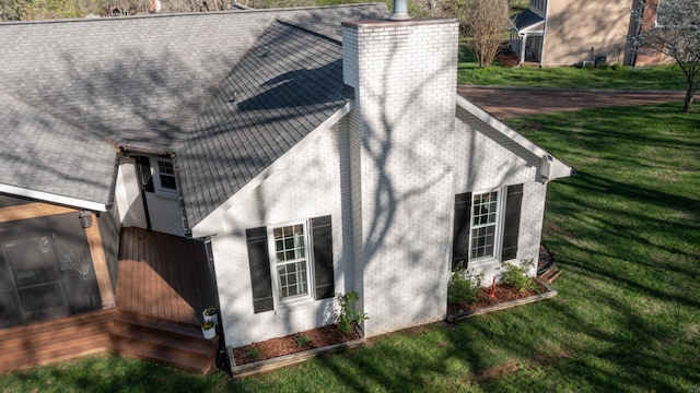 view of side of property featuring roof with shingles, a chimney, and a yard
