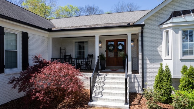 doorway to property with a porch, a shingled roof, and brick siding
