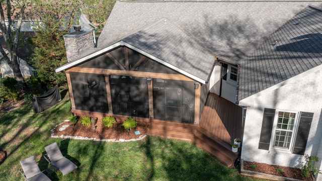 back of house featuring a yard, a chimney, a sunroom, and roof with shingles