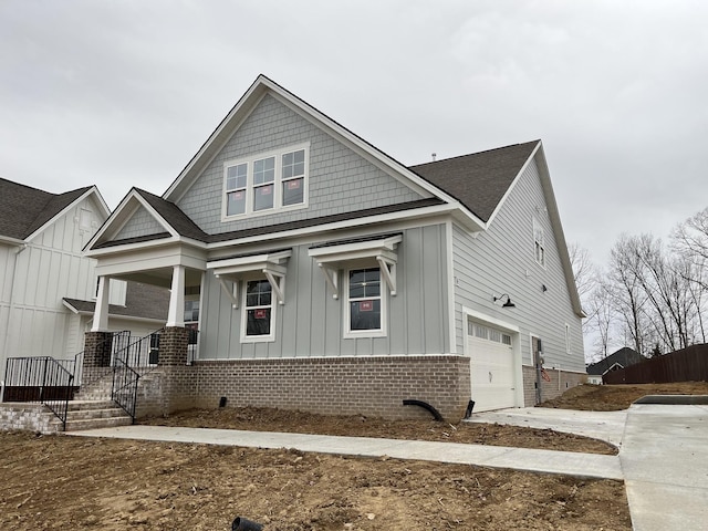 view of front of house with covered porch, an attached garage, concrete driveway, board and batten siding, and brick siding