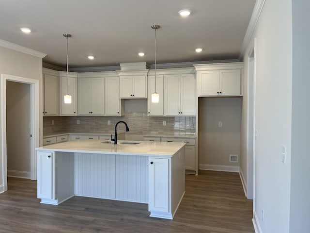 kitchen with a sink, ornamental molding, baseboards, and a center island with sink