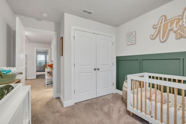 bedroom featuring visible vents, a closet, a crib, and light carpet