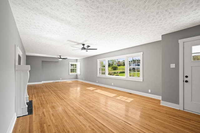 unfurnished living room with light wood-style flooring, a textured ceiling, baseboards, and a ceiling fan