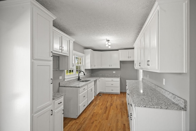 kitchen featuring light wood-type flooring, light stone counters, a textured ceiling, white cabinets, and a sink