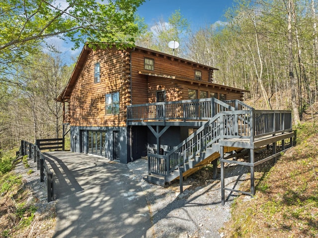 back of property featuring log exterior, an attached garage, stairway, a wooden deck, and driveway