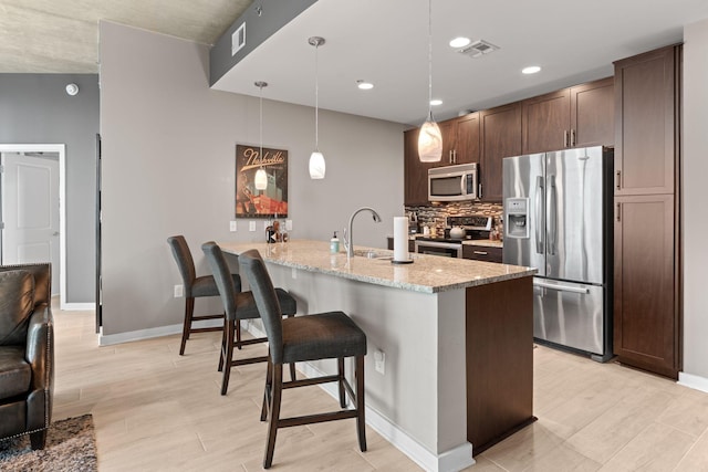 kitchen with a peninsula, a breakfast bar, appliances with stainless steel finishes, light stone counters, and baseboards