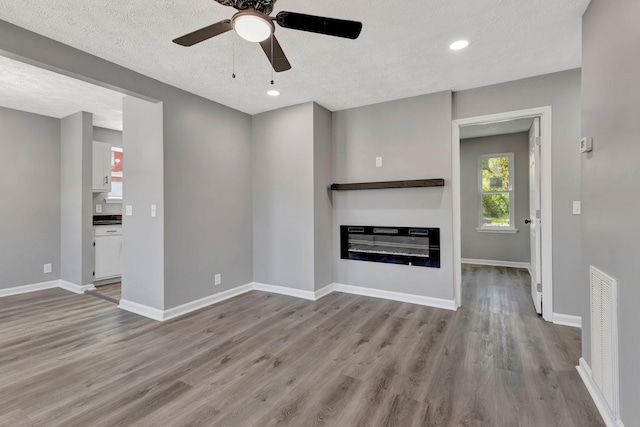 4817 Terragon Trl, Antioch, TN 37013 - unfurnished living room with wood finished floors, baseboards, a glass covered fireplace, a textured ceiling, and ceiling fan