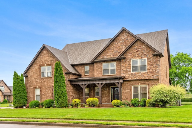 craftsman-style house featuring brick siding, a shingled roof, a front lawn, and covered porch