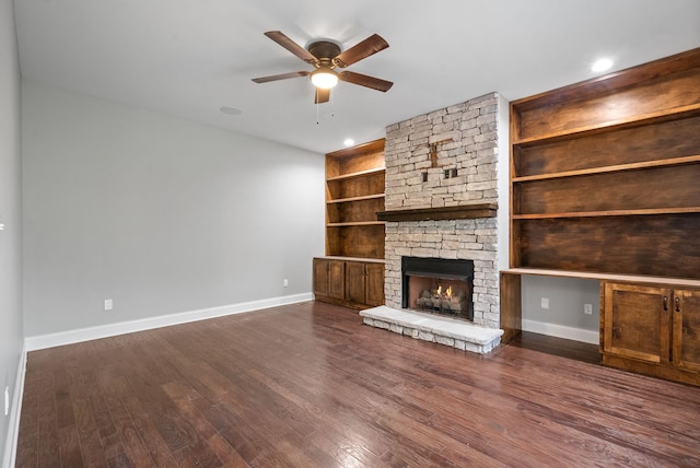 unfurnished living room featuring baseboards, ceiling fan, dark wood-style flooring, and a stone fireplace