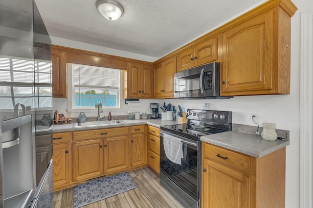 kitchen featuring a sink, light countertops, a textured ceiling, light wood finished floors, and stainless steel appliances