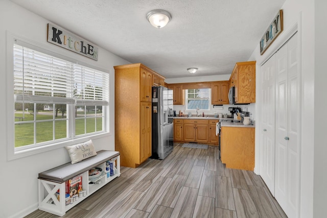 kitchen with a textured ceiling, light countertops, wood tiled floor, appliances with stainless steel finishes, and a sink