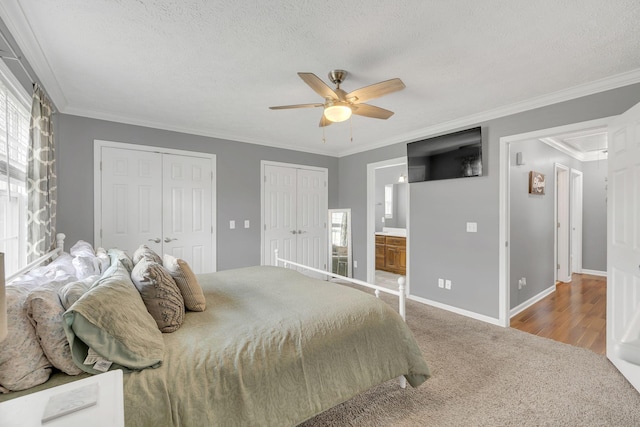 carpeted bedroom with baseboards, a textured ceiling, multiple closets, and ornamental molding