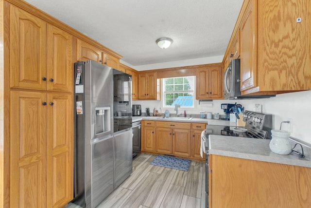 kitchen featuring a textured ceiling, light countertops, a sink, stainless steel appliances, and light wood finished floors