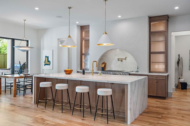 kitchen with decorative backsplash, recessed lighting, a large island with sink, and light wood-type flooring