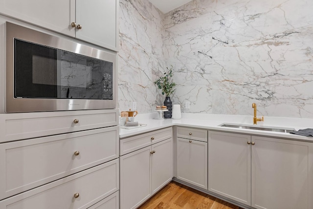 kitchen featuring built in microwave, light countertops, light wood finished floors, and a sink