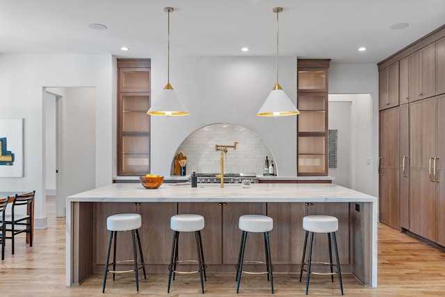 kitchen featuring a large island, backsplash, light wood-style floors, light stone counters, and a breakfast bar