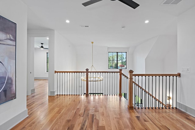 hallway with an upstairs landing, wood finished floors, visible vents, and recessed lighting