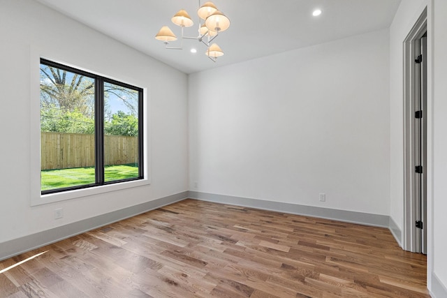 empty room with baseboards, wood finished floors, a chandelier, and recessed lighting