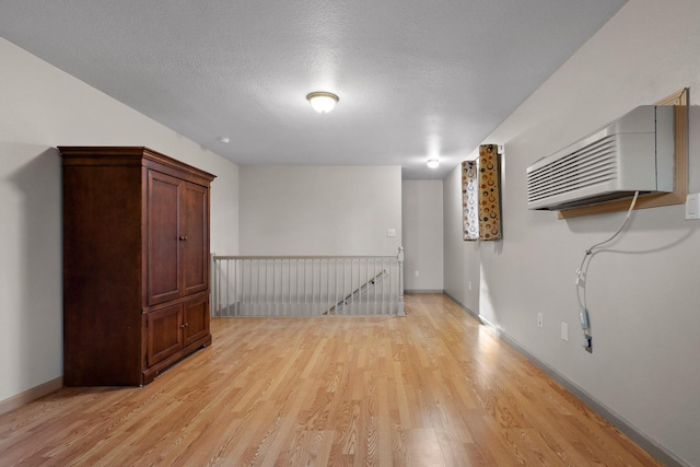 basement featuring baseboards, a wall mounted AC, light wood-style floors, and a textured ceiling