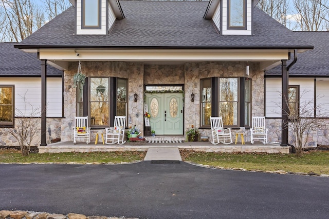 doorway to property with stone siding, a shingled roof, and covered porch