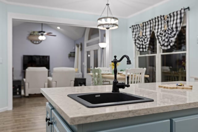 kitchen featuring pendant lighting, ceiling fan with notable chandelier, light stone countertops, wood finished floors, and a sink