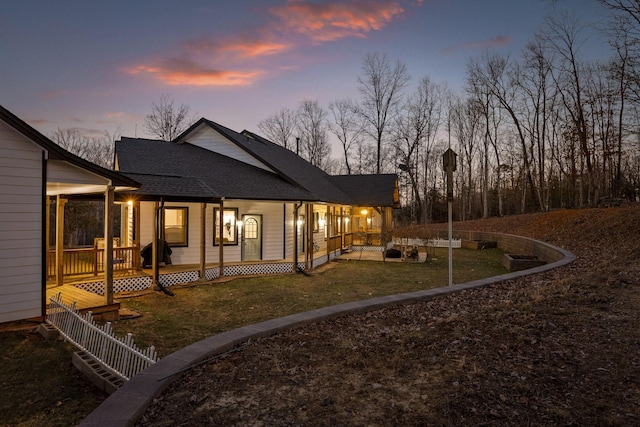 back of property at dusk featuring a shingled roof, fence, and a lawn