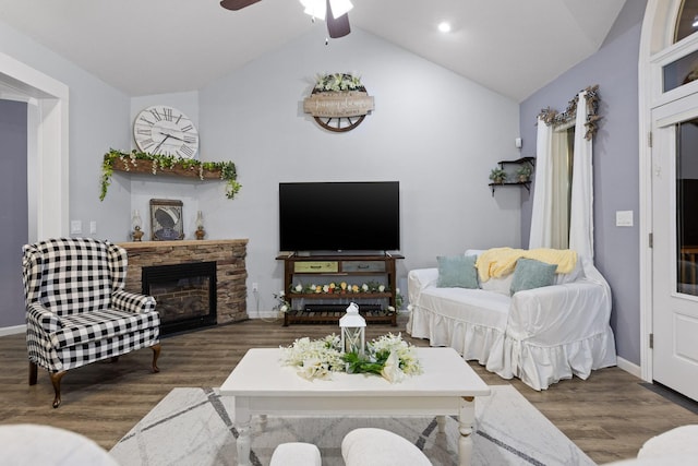 living area featuring wood finished floors, baseboards, a stone fireplace, and lofted ceiling