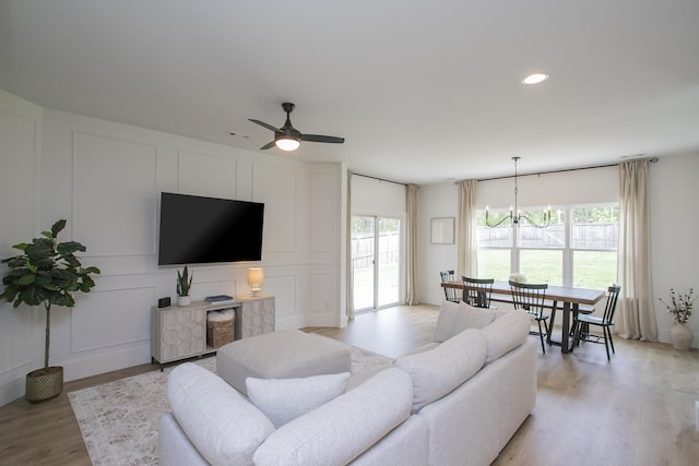 living area featuring ceiling fan with notable chandelier, recessed lighting, light wood-style floors, and a decorative wall
