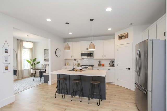 kitchen with white cabinets, light countertops, a sink, decorative backsplash, and appliances with stainless steel finishes